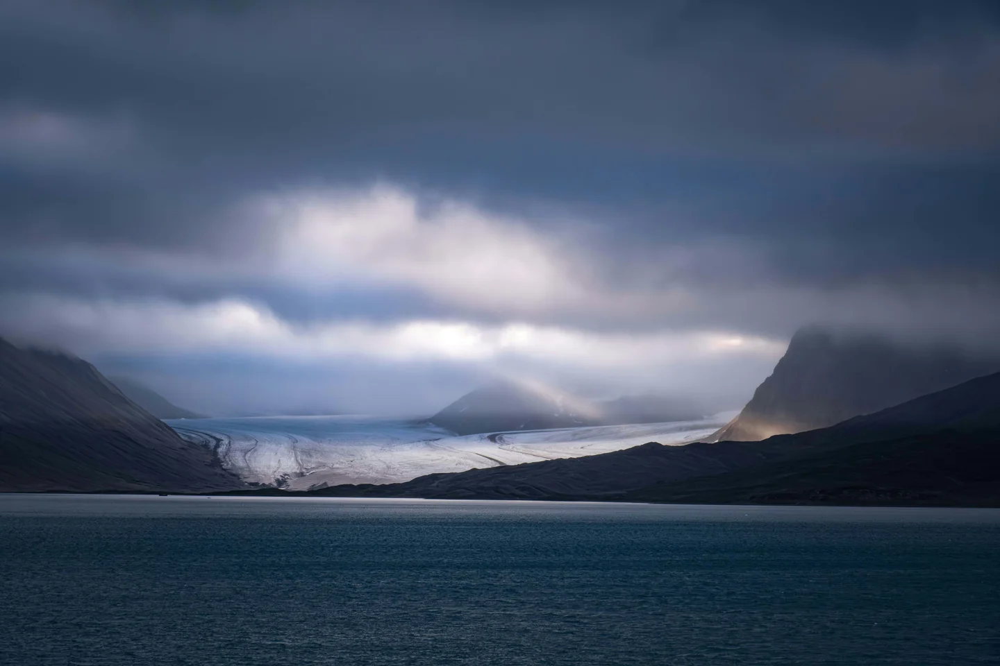 A glacier between dark mountains under low clouds in Svalbard