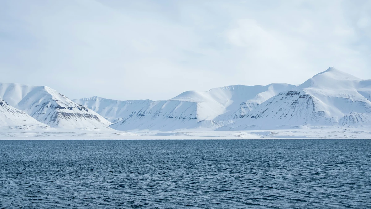 Snow-covered coastal mountains stretch above dark blue water under a pale sky.