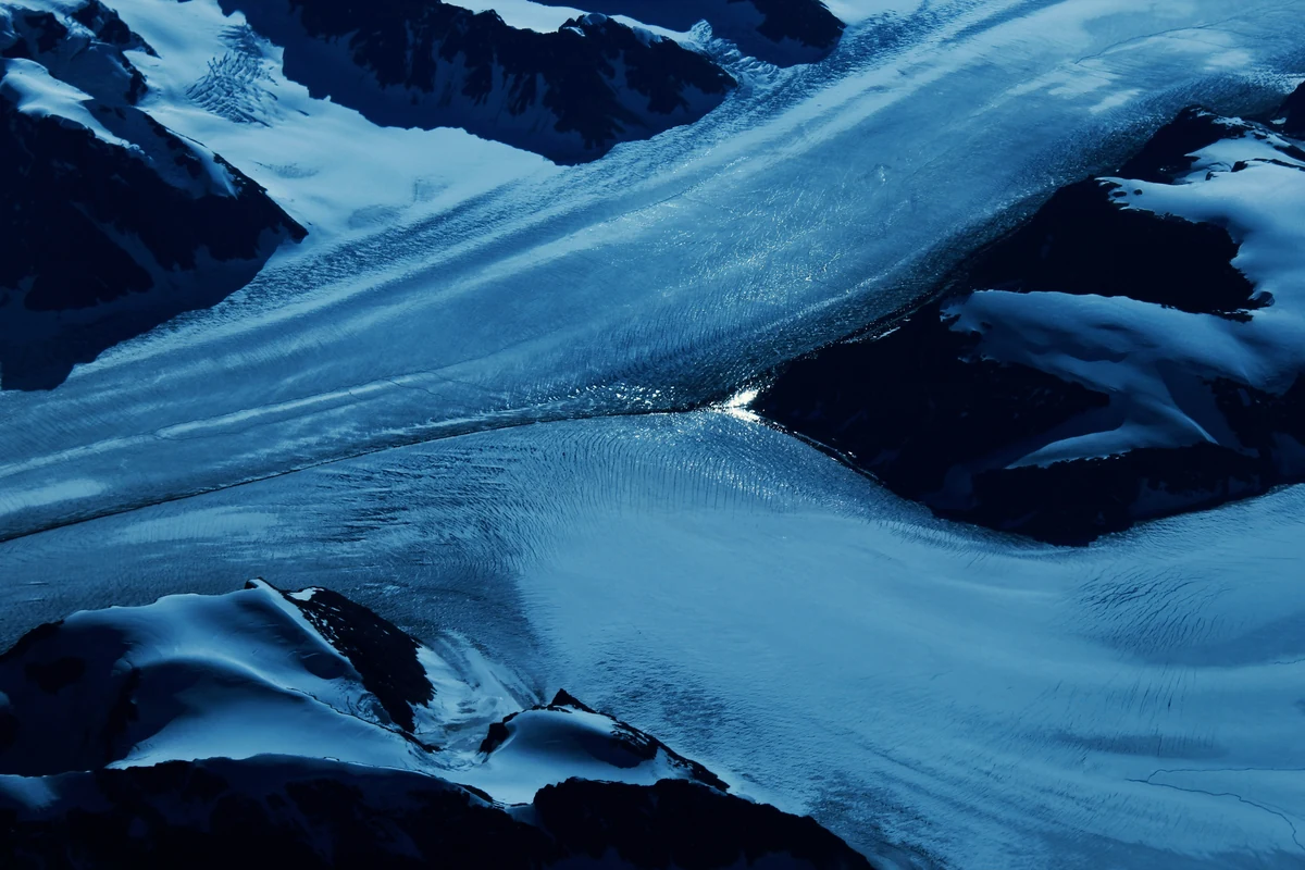 Blue glacial ice winds between dark, snow-covered mountain ridges.
