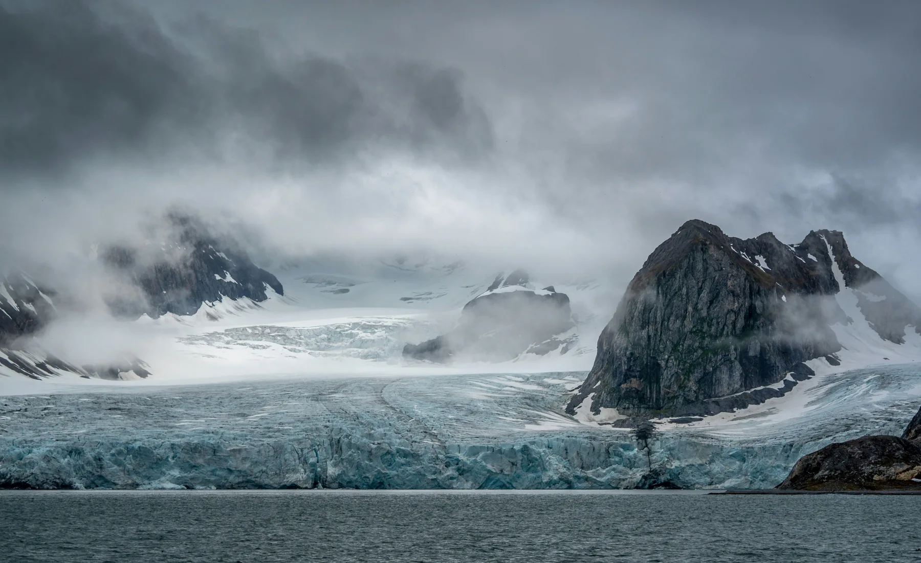 A glacier descending between rocky mountains towards the water